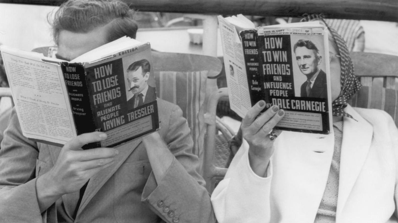 A man and a woman seated in deck chairs read contrasting How To books