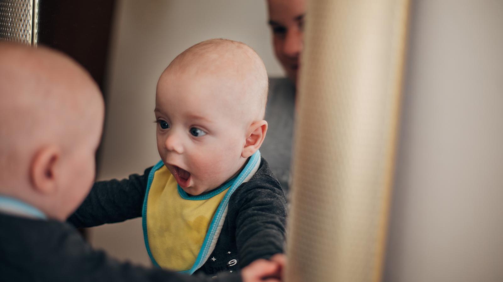 Baby looking at itself in the mirror with a surprised expression