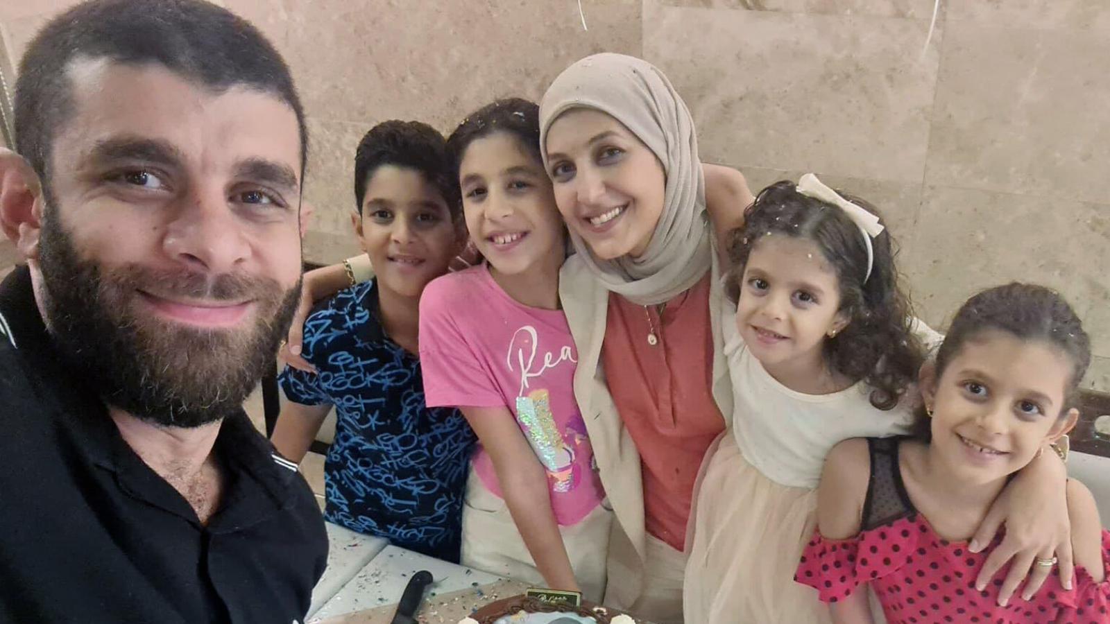 A family. Mother and four children with arms around each other, dad in foreground taking the family selfie.