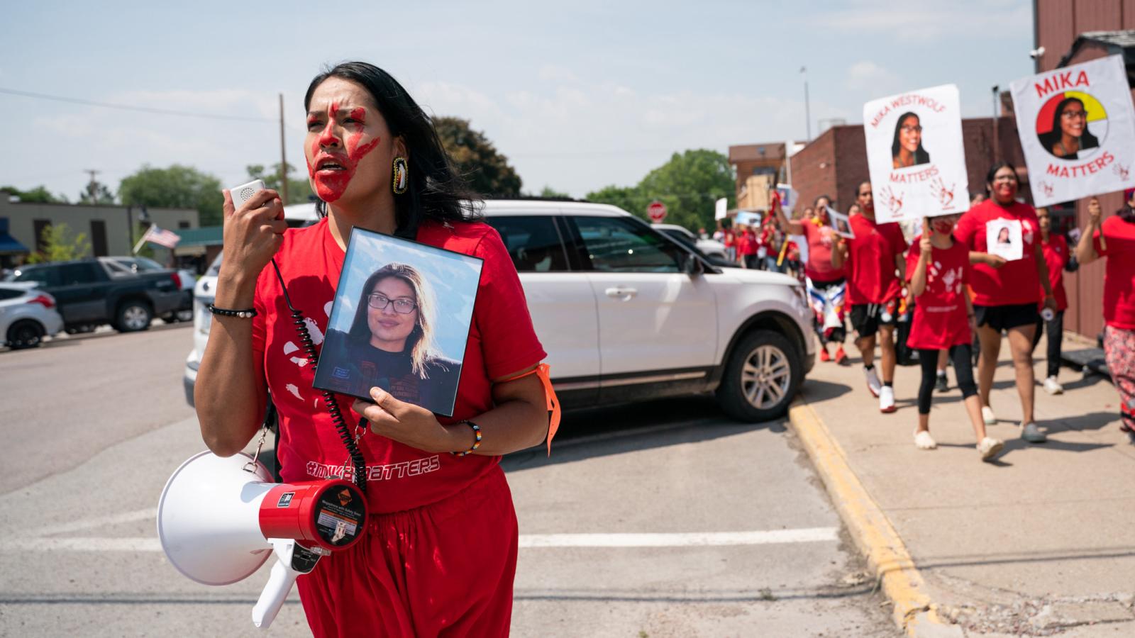 A woman is protesting while holding a photo of a young girl