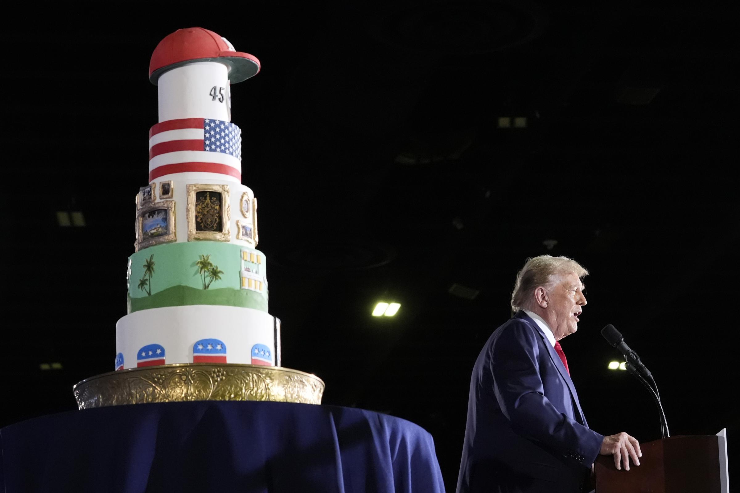 Donald Trump speaks at his birthday celebration next to a big multi-tiered cake