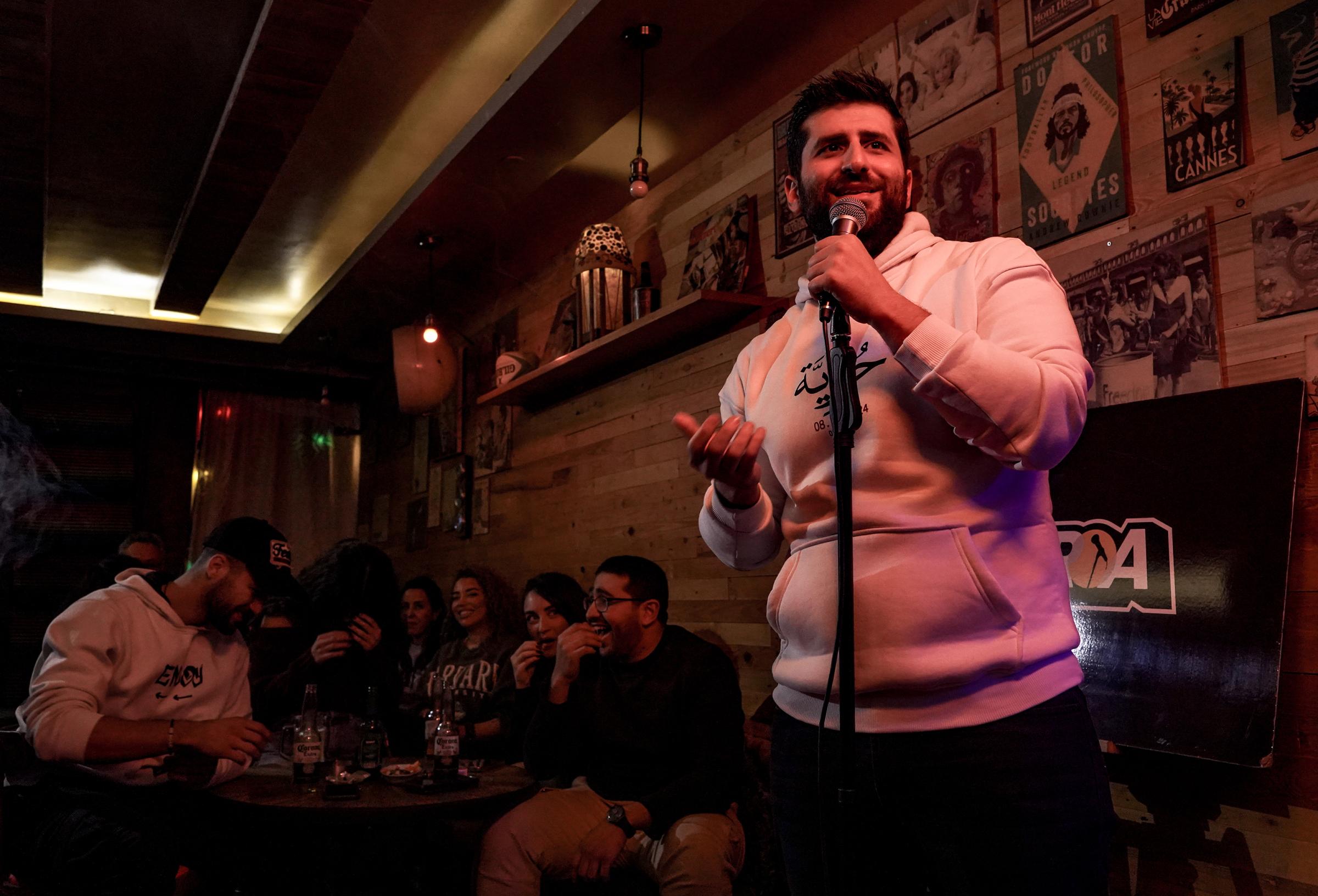 Photo of a comedian on stage with a mic and people at a table laughing